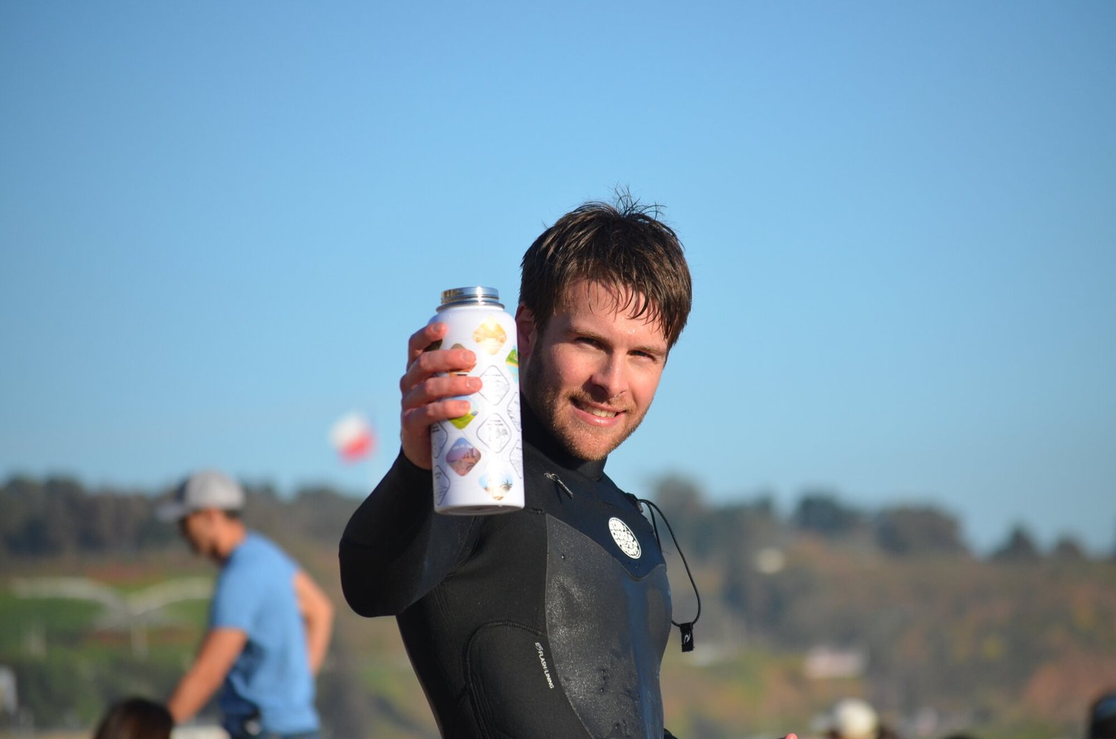 Surfista mostrando la botella Kalpu, mirando a cámara